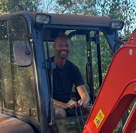 Johan Hoekstra lachend in de cabine van een minigraver